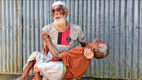 শেরপুরে এক প্রবীণ মানুষ আরেকজন অসহায়কে কোলে নিয়ে দাঁড়িয়ে আছেন